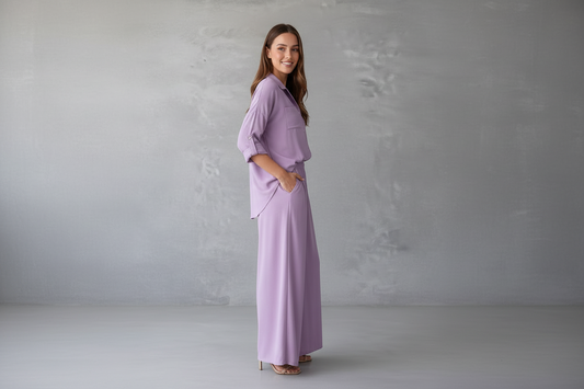 Woman wearing a lavender outfit standing against a plain gray background