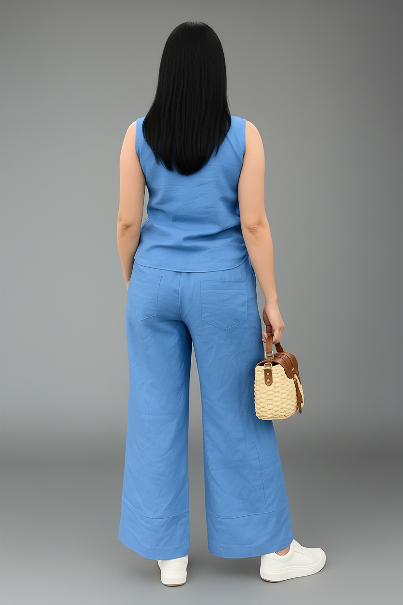 Person wearing a blue sleeveless top and wide-leg pants, holding a straw bag on a gray background