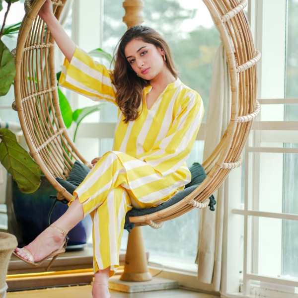 Woman in yellow and white striped outfit sitting in a hanging chair indoors.
