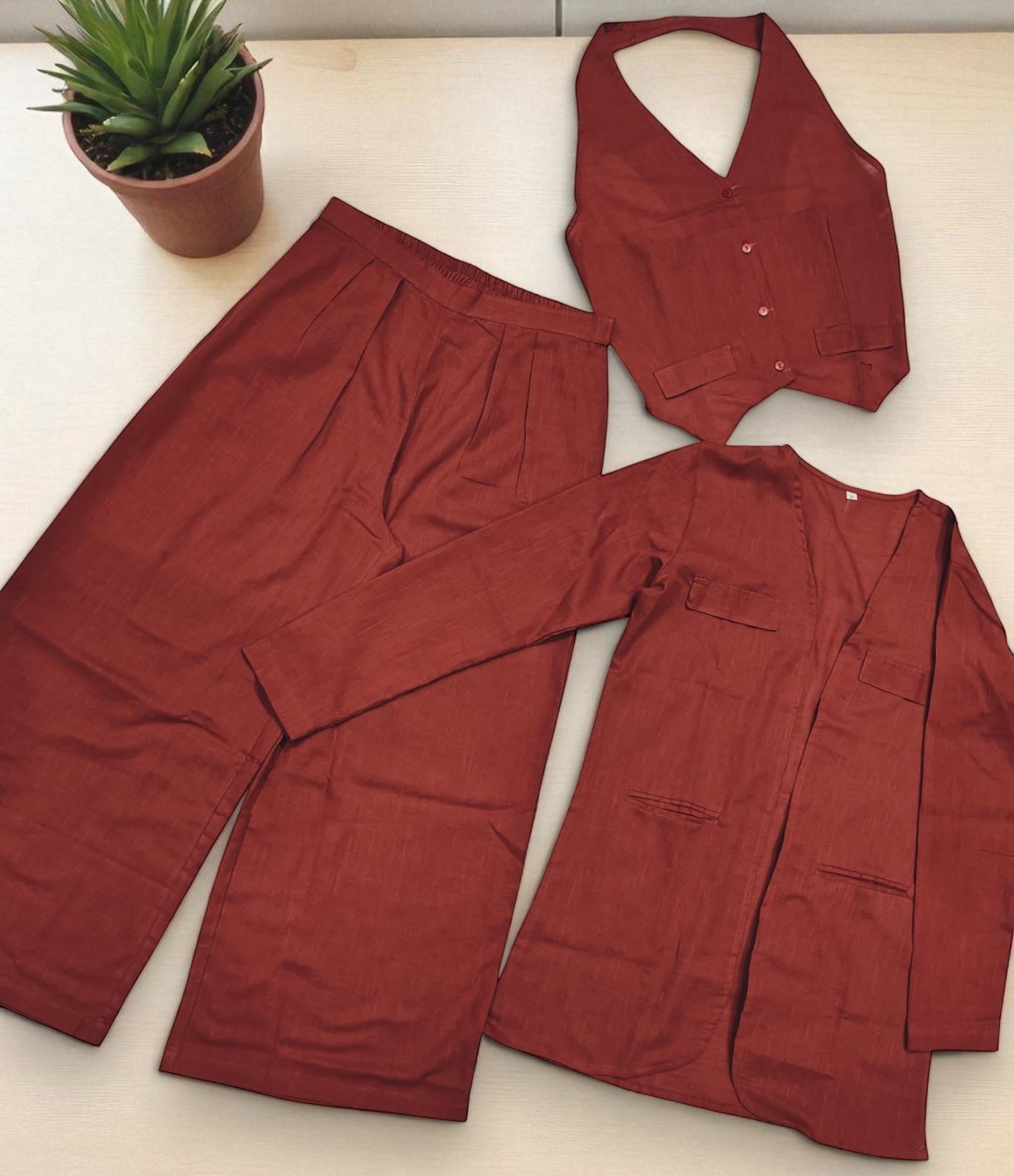 Red pajama set with matching vest on a light surface, next to a potted plant.