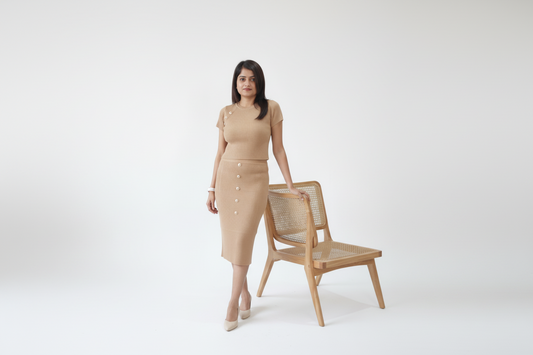 Woman in a beige dress standing next to a wooden chair on a white background