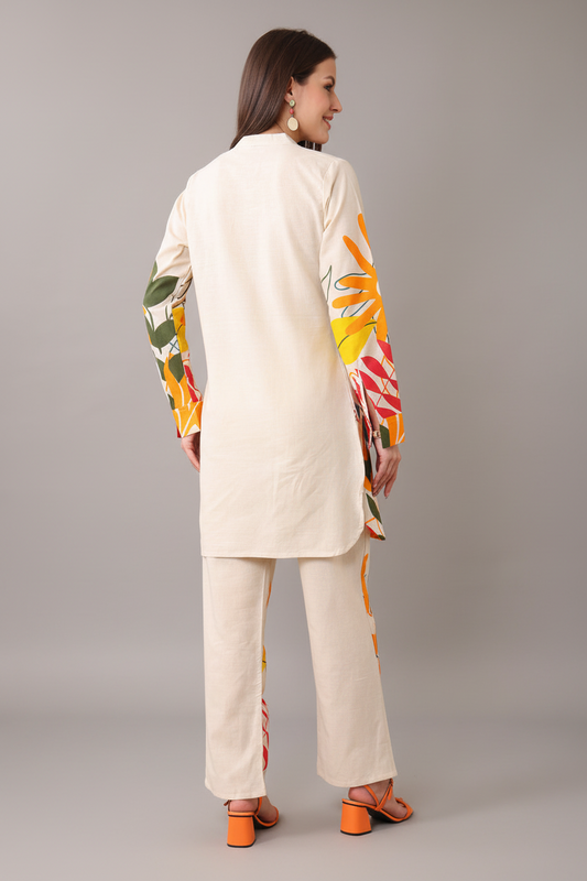 Woman wearing a cream-colored outfit with colorful floral patterns on a gray background