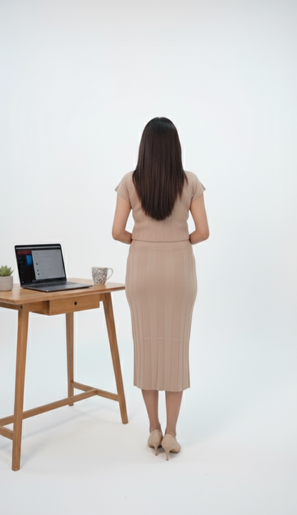 Back image of Woman wearing beige ribbed co-ord set with pearl button detailing, featuring a fitted crop top and midi pencil skirt, styled with nude flats against a brown background.