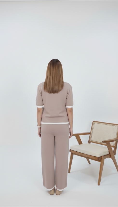 Back image of Woman wearing taupe knit co-ord set with pearl-button front top and white trim, paired with matching straight-fit pants, posing indoors beside a keyboard.