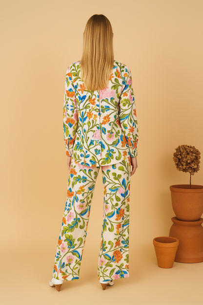 Woman wearing a colorful floral outfit standing against a beige background with potted plants.