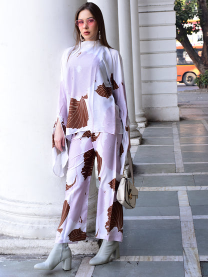 Woman in a stylish outfit with a patterned top and pants standing against a building.