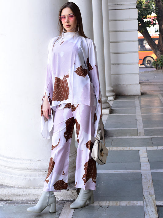 Woman in a stylish outfit with a patterned top and pants standing against a building.
