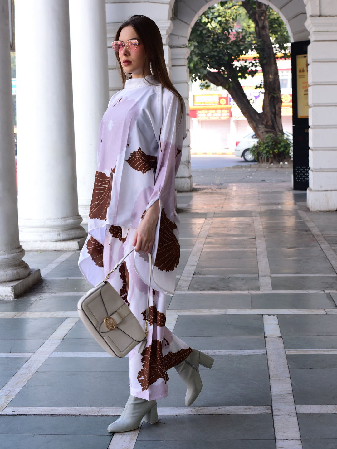 Woman in a white and brown patterned outfit standing in an outdoor setting with columns.