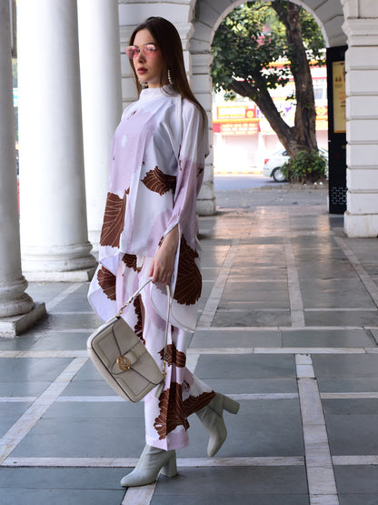 Woman in a white and brown patterned outfit standing in an outdoor setting with columns.