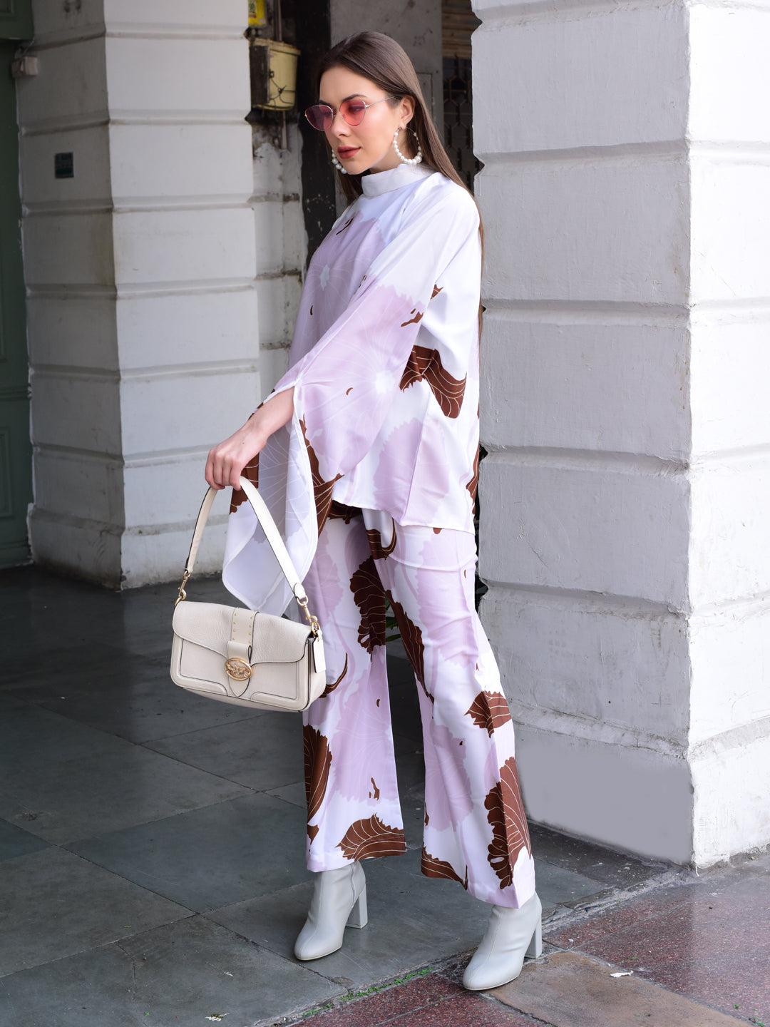 Woman in a stylish outfit with a white handbag standing against a building.