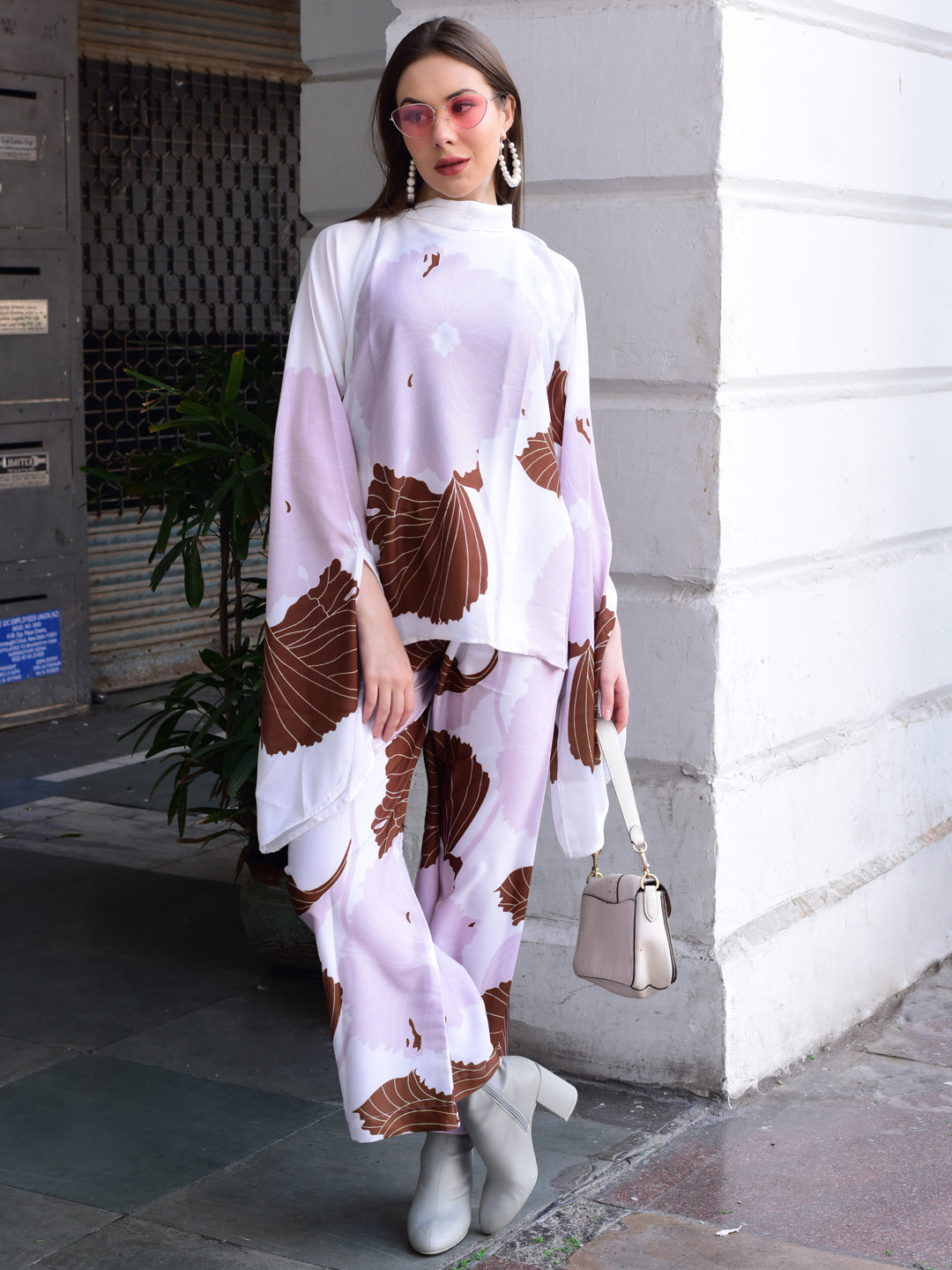 Woman wearing a white and brown patterned outfit with a beige handbag on a city street.