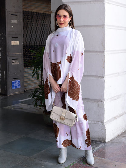 Woman wearing a white dress with brown patterns, holding a beige handbag, standing on a sidewalk.