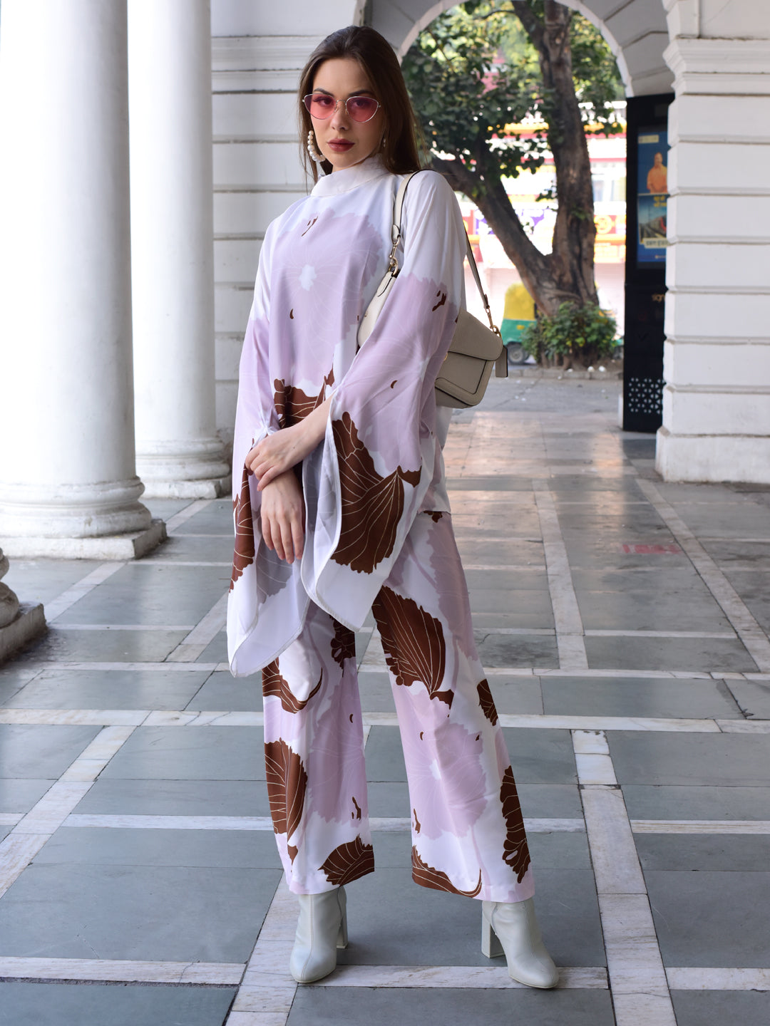 Woman in a patterned outfit standing in an outdoor setting with columns and greenery.
