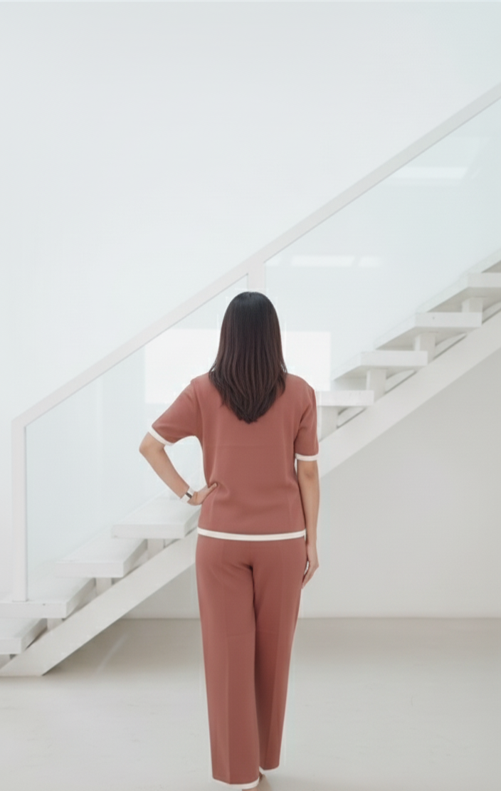Woman wearing Brown knit co-ord set with pearl-button front top and white trim, paired with matching straight-fit pants, posing indoors beside a keyboard.