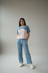 Woman wearing a two-tone top and light blue pants against a plain background