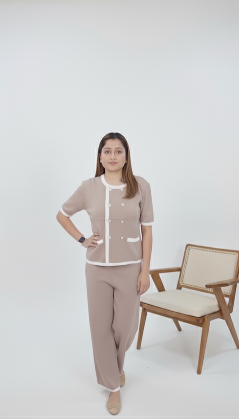 Woman wearing taupe knit co-ord set with pearl-button front top and white trim, paired with matching straight-fit pants, posing indoors beside a keyboard.