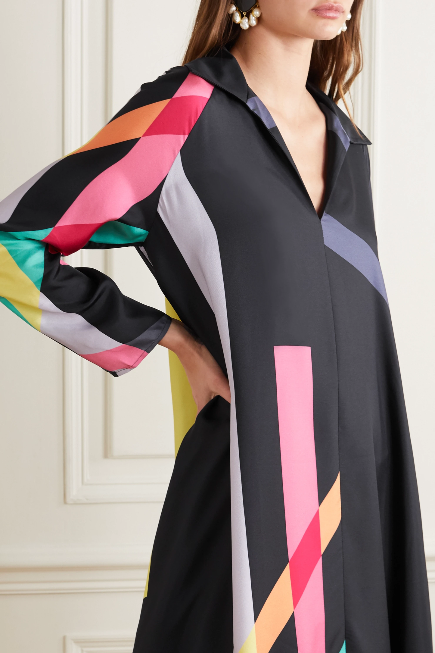 Black dress with colorful striped sleeves worn by a model against a white wall.