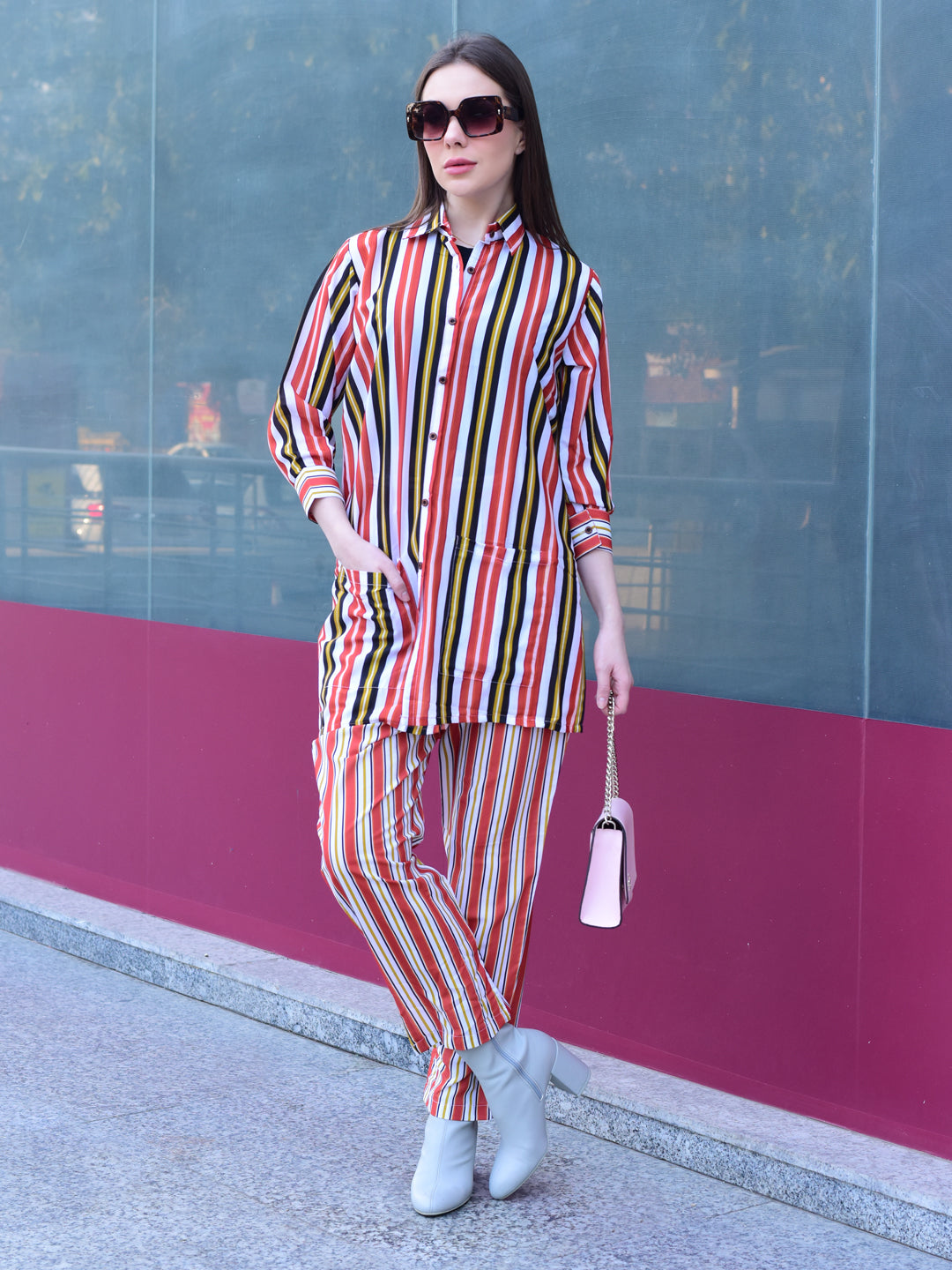 Woman in a colorful striped outfit standing against a glass wall with a pink base, stylish and versatile co-ord set for women 